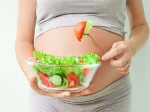 donna incinta tiene una ciotola con insalata e pomodori per il pasto