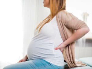 Donna in stato di gravidanza seduta si tiene la schiena e si riposa