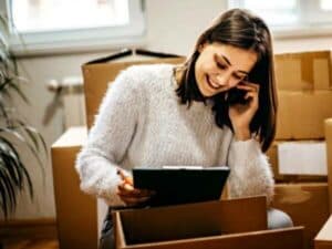 ragazza con cellulare e scatoloni sullo sfondo per organizzare il trasloco